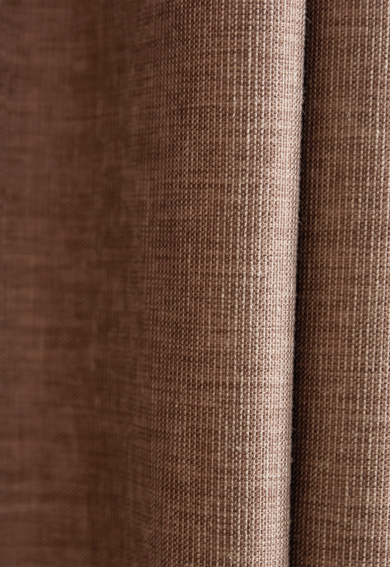 Nærbilde av et brunt gardinstoff med tekstur, som viser fine vevde detaljer og naturlige folder i materialet.
