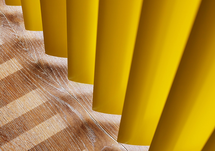Nærbilde av lysegule vertikale persienner som kaster stripete skygger på et tregulv.