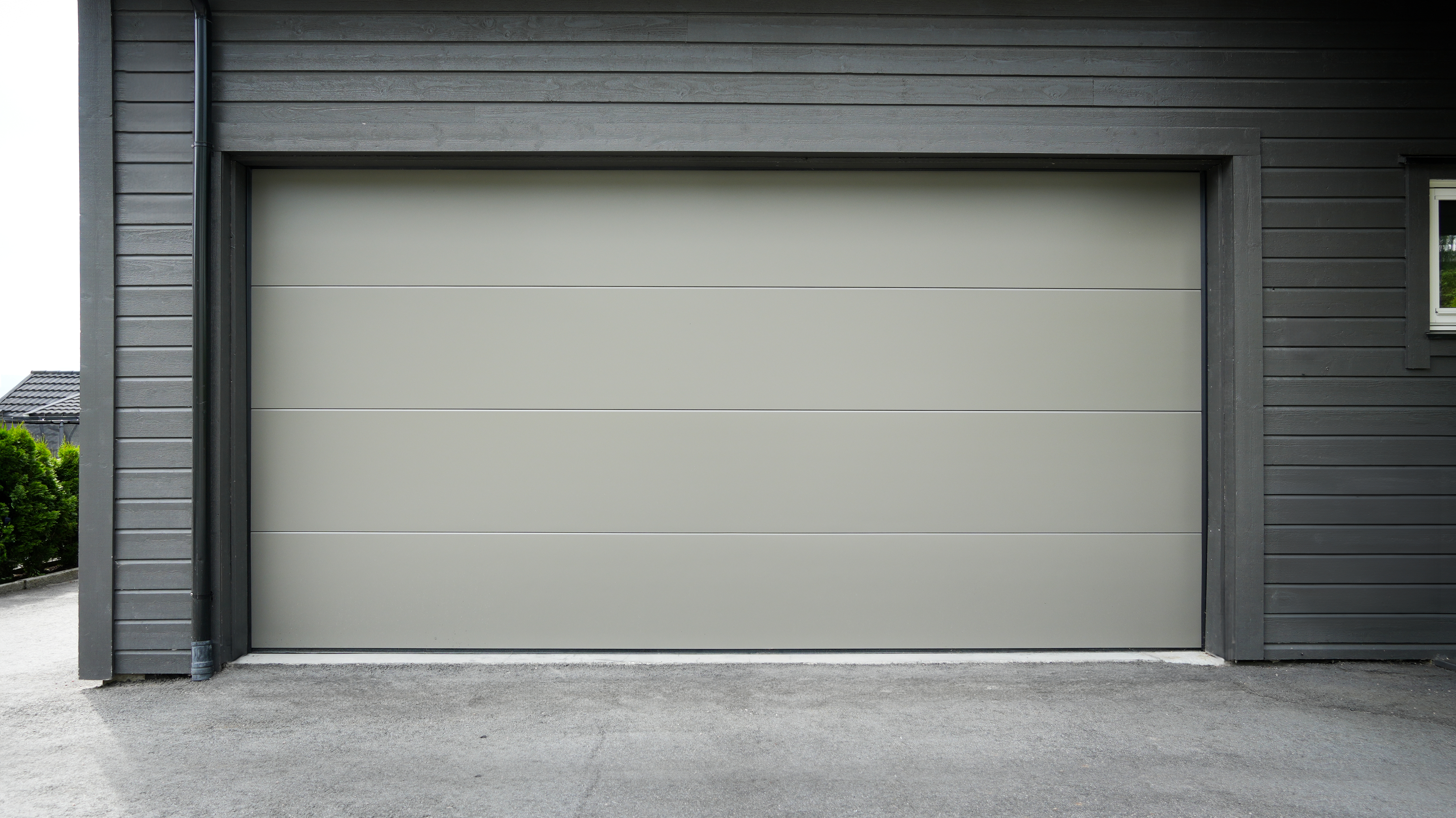 Moderne garasje med en elegant lysegrå seksjonsport i en yttervegg av mørkt treverk.
