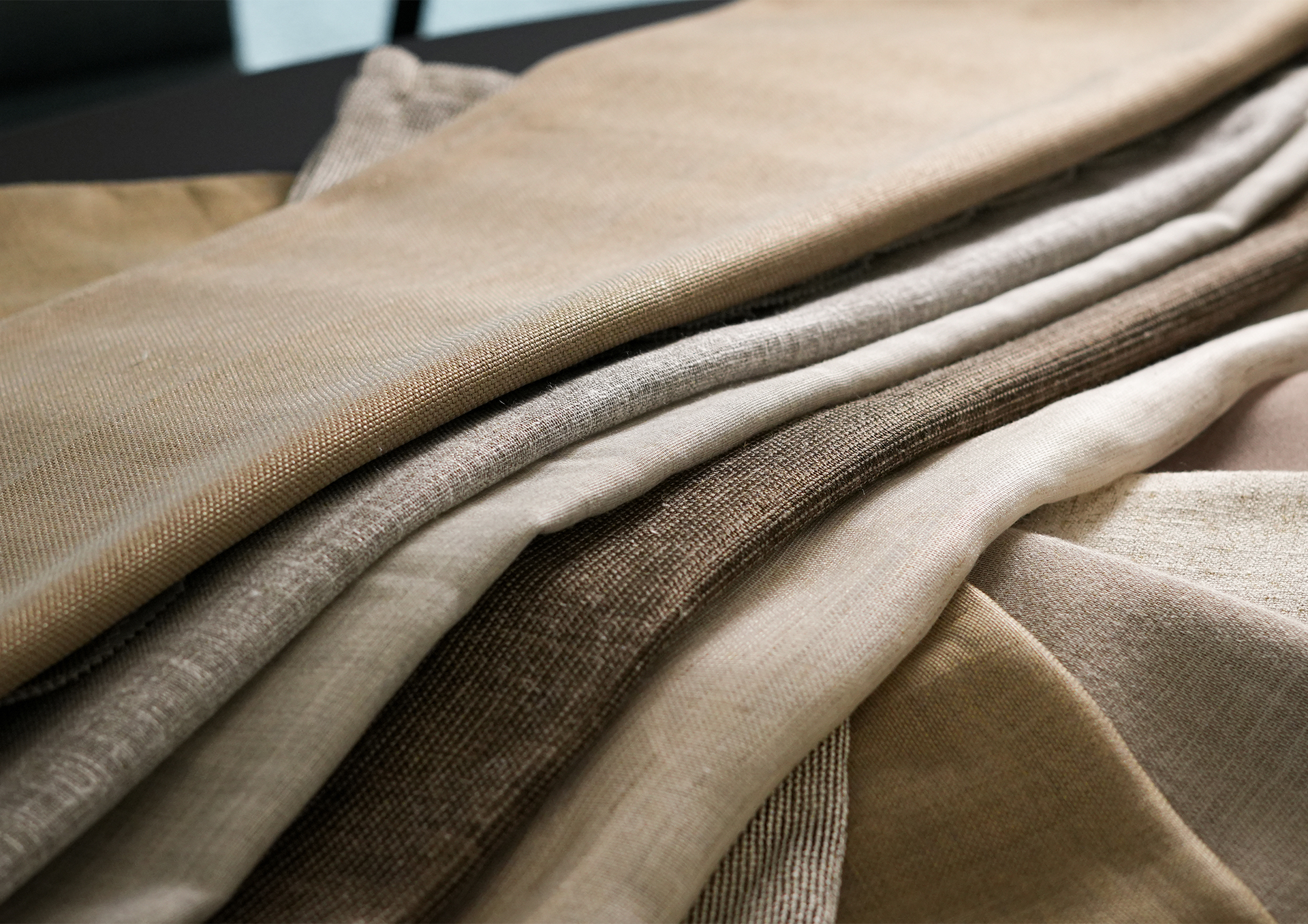 Nærbilde av lagdelte tekstilprøver i nøytrale beige og brune toner, som viser myke teksturer og vevde mønstre.