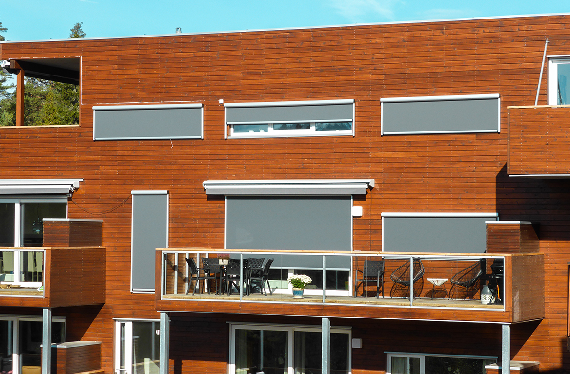 Moderne leilighetsbygg i tre med grå utvendige persienner og balkonger møblert med utemøbler.