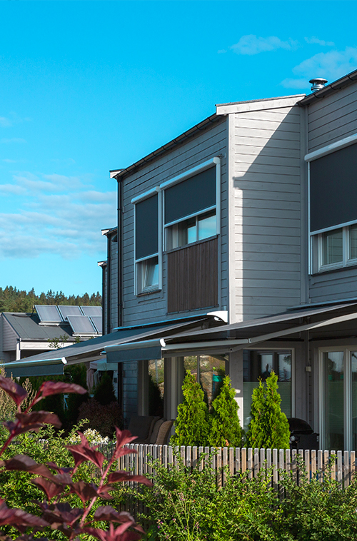 Moderne rekkehus med grå utvendige persienner, balkong og markiser som gir skygge til terrassen i et grønt nabolag.