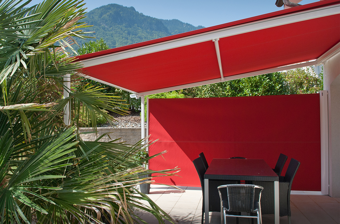 Terrasse med rød markise og matchende levegg, med sorte utemøbler og utsikt mot fjellene.