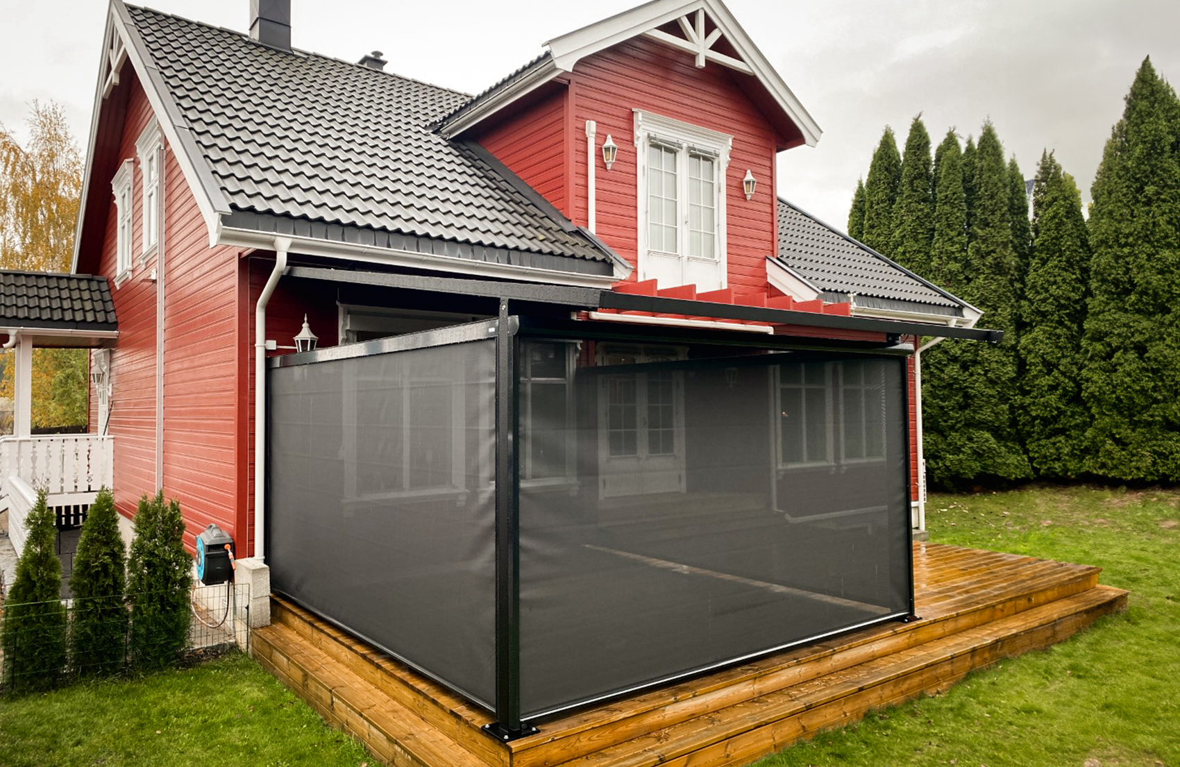 Rødt trehus med grått tak og innglasset terrasseområde med sorte nettingbaserte avskjerminger.
