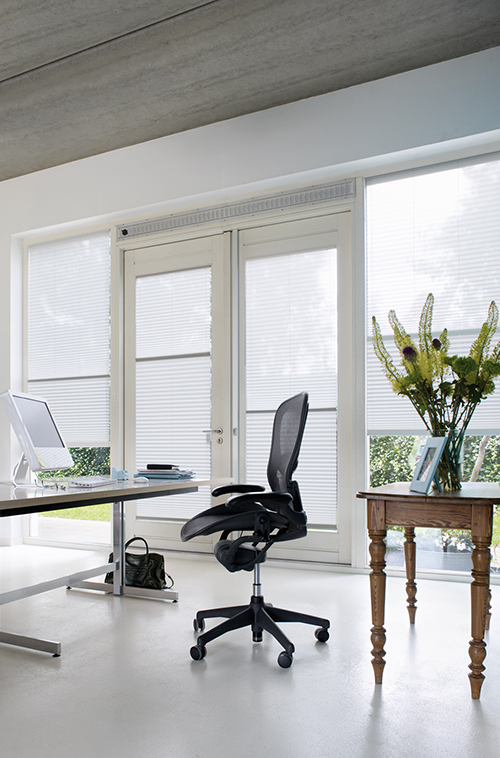 Moderne hjemmekontor med hvite vegger, store vinduer med hvite gardiner, skrivebord, kontorstol og friske blomster.