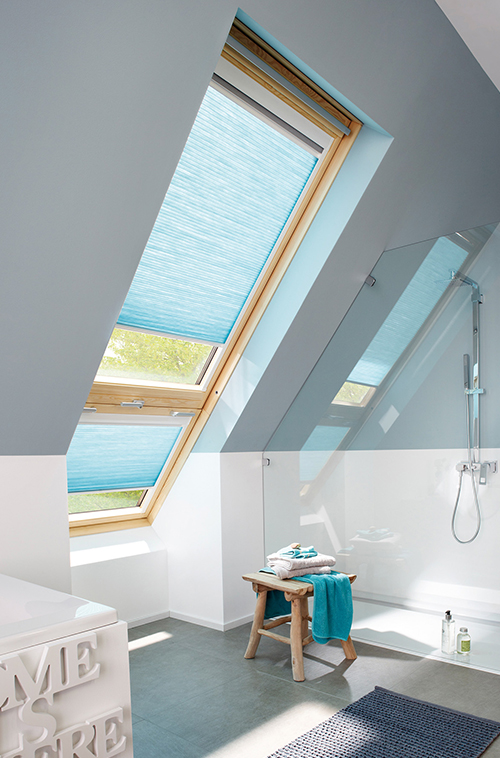 Loftsbaderom med takvinduer utstyrt med blå gardiner, dusjområde og krakk i tre.
