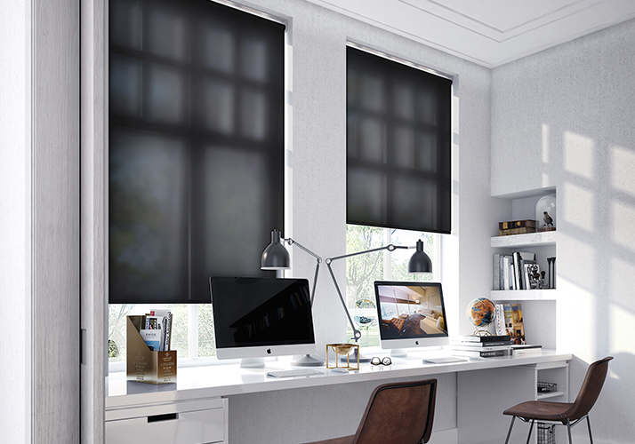 Moderne kontor med hvitt skrivebord, to datamaskiner og store vinduer med svarte rullegardiner.