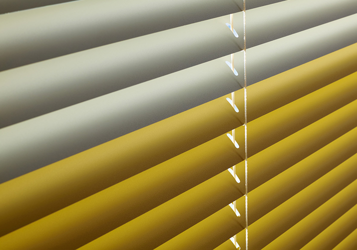 Detaljert visning av gule horisontale persienner med mykt lys som filtrerer gjennom lamellene.