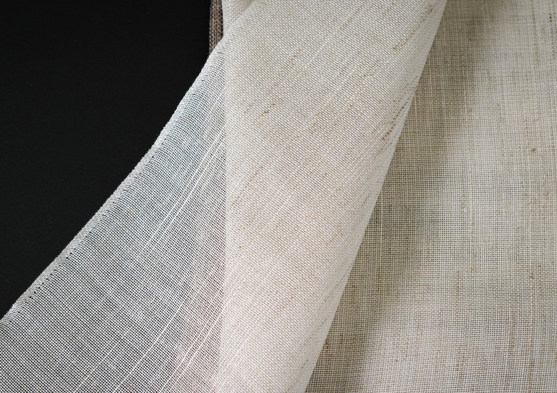 Nærbilde av lett, gjennomsiktig gardinstoff med delikat vevet tekstur mot mørk bakgrunn.