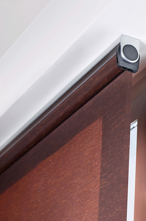 Nærbilde av en brun rullegardin med sølvfarget monteringsbrakett som viser stoffet og monteringsdetaljene.