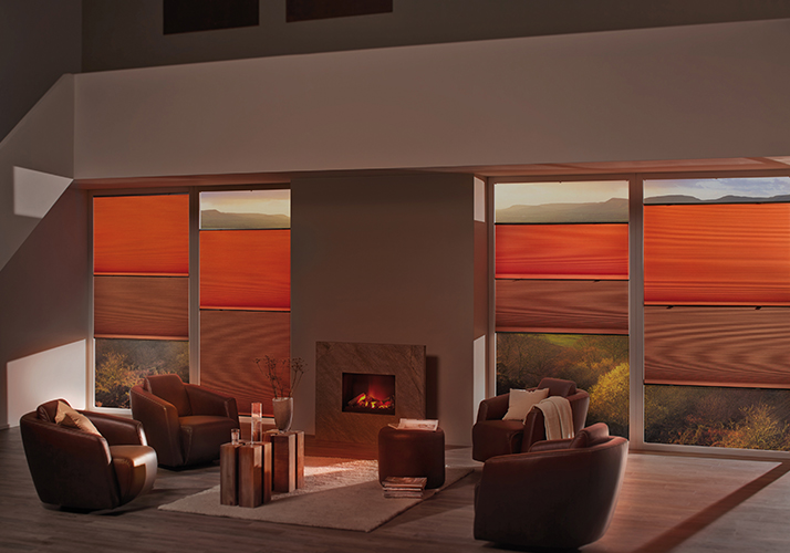 Stue med varm belysning, skinnstoler og rød-oransje gardiner som rammer inn en peis og store vinduer.