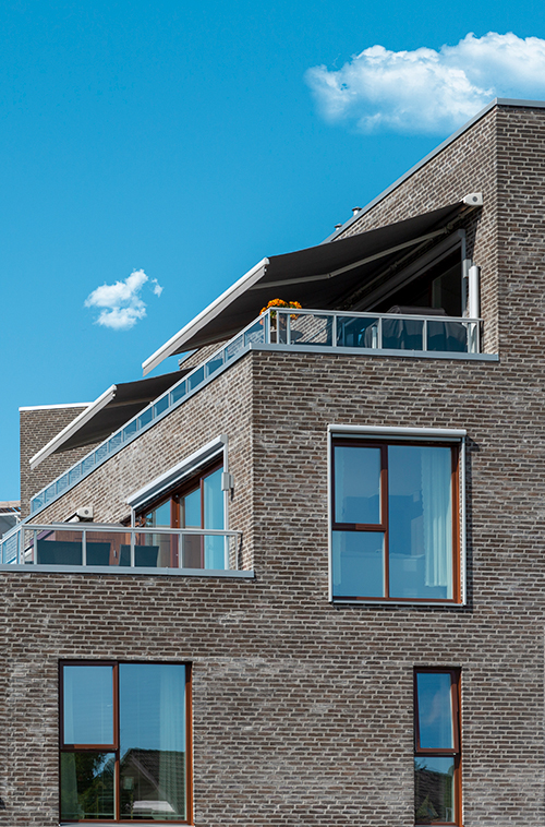 Et moderne betonghus med skråtak og rektangulære vinduer, under en klar blå himmel med én enkelt sky.