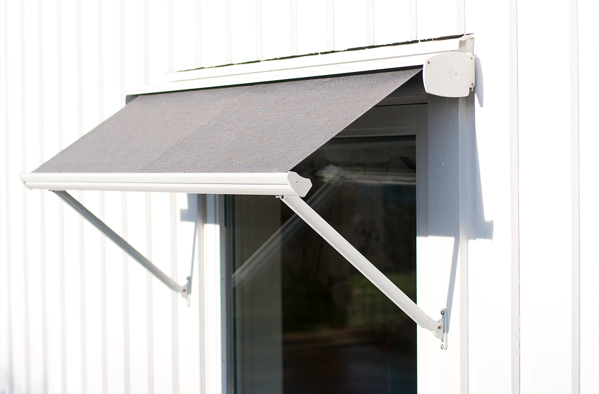 Liten moderne vindusmarkise med grått stoff og hvit ramme, montert på en vegg med hvit kledning for solbeskyttelse.