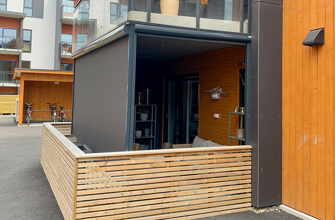 Hjørne av utendørs terrasse med grå uttrekkbar screen og tregjerde, som skaper et skyggefullt og privat rom.